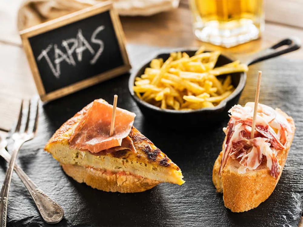 Từ “tapas” trong tiếng Tây Ban Nha có nghĩa là “đậy” hoặc “che phủ”